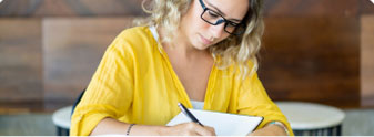 A woman in a yellow shirt taking notes to master the craft of writing and book outlining.